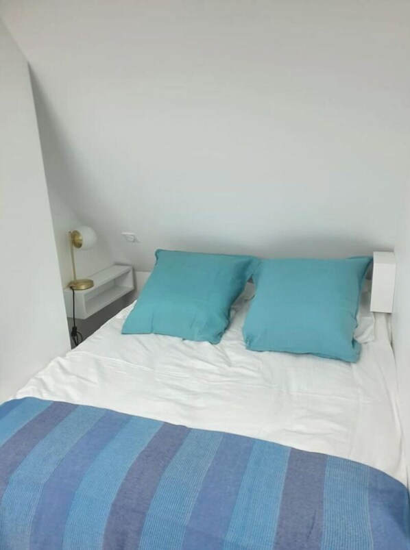 Ein Schlafzimmer mit einem Bett, zwei Kissen, einem Nachttisch mit einer Lampe und einer gestreiften Decke.