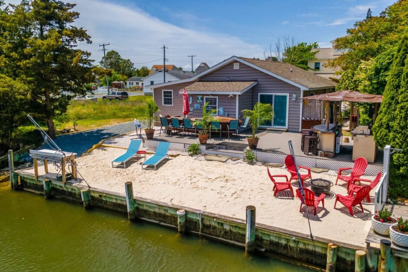 Een huis met een patio van zand, buitenmeubels en een steiger die in het water uitloopt.