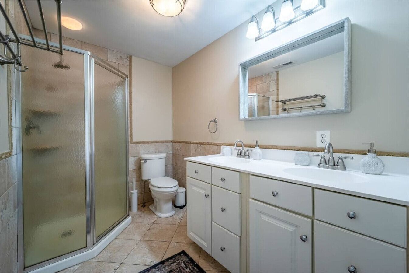 A bathroom with a glass shower enclosure, a toilet, a sink with a mirror above, and a vanity with drawers.