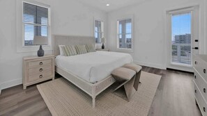 Une chambre à coucher avec un grand lit, des tables de chevet, une commode et une fenêtre avec des stores.