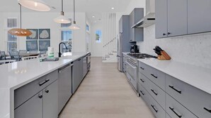 Una cocina moderna con gabinetes grises, encimera blanca e iluminación colgante.