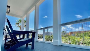Un espacio al aire libre cubierto con terraza de madera, una banca y vistas a un paisaje urbano y palmeras.