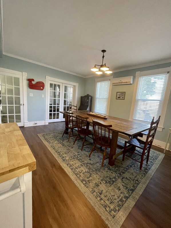 A dining room with a wooden table and chairs, a rug, and a ceiling light fixture.