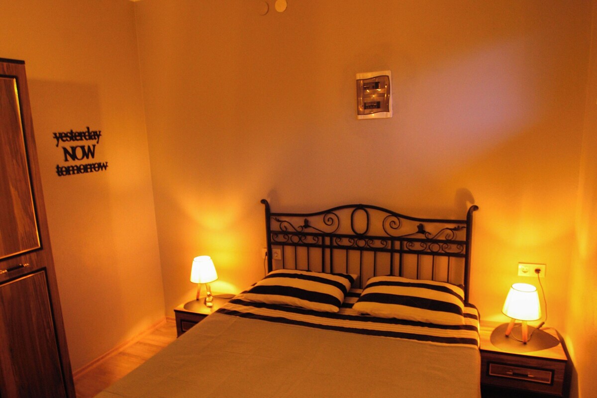 A bedroom with a bed, two bedside lamps, a wall clock, and a door.