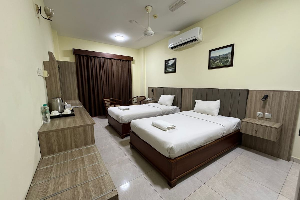 A hotel room with two beds, a desk, a chair, an air conditioner, and a window with curtains.
