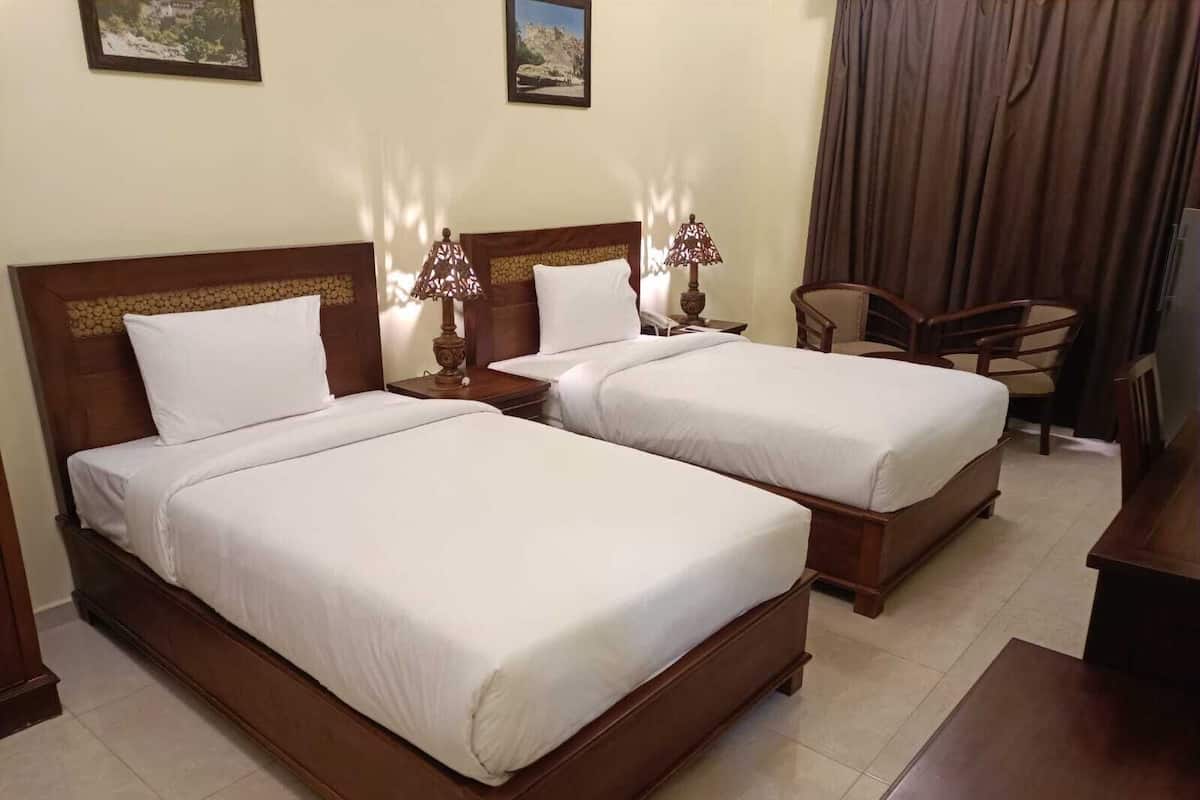 A hotel room with two wooden beds, a chair, a desk, and a lamp.