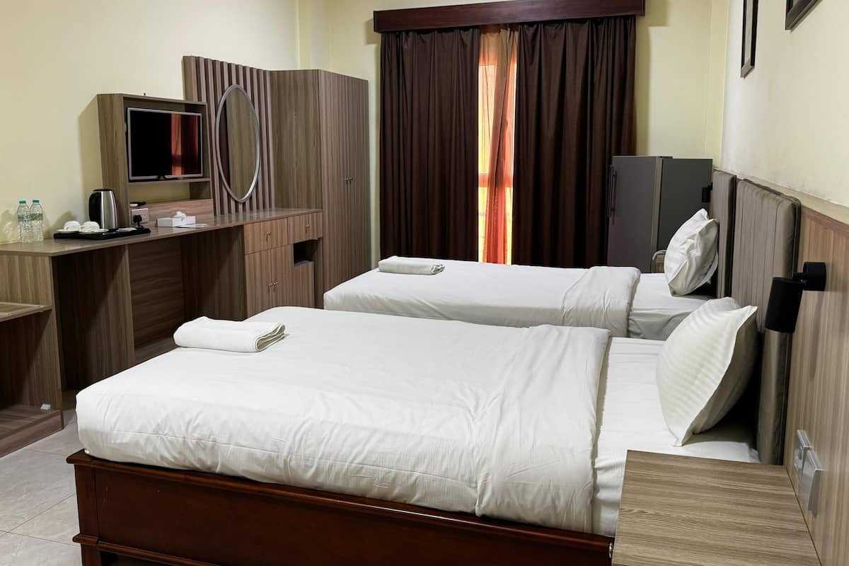 A hotel room with two beds, a desk with a TV, a mirror, and a wardrobe.
