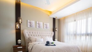 Una habitación de hotel moderna con una cama grande, una mesita de noche, una lámpara de pared y un ventanal con cortinas traslúcidas.