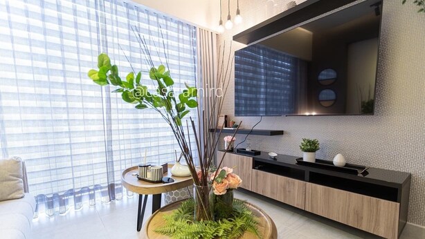 Una sala de estar moderna con una mesa redonda de madera, un sofá, un televisor montado en la pared y una ventana con persianas.