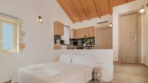 A bedroom with a bed, a small bedside table, a window, and a view of a kitchen.