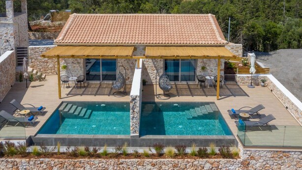 A two-story villa with a swimming pool, outdoor seating, and a stone facade.