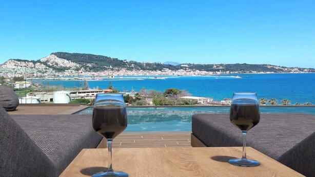 Due bicchieri di vino su un tavolo di legno con vista su una località costiera e sul mare.