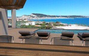 A poolside area with lounge chairs and a view of the sea and town.