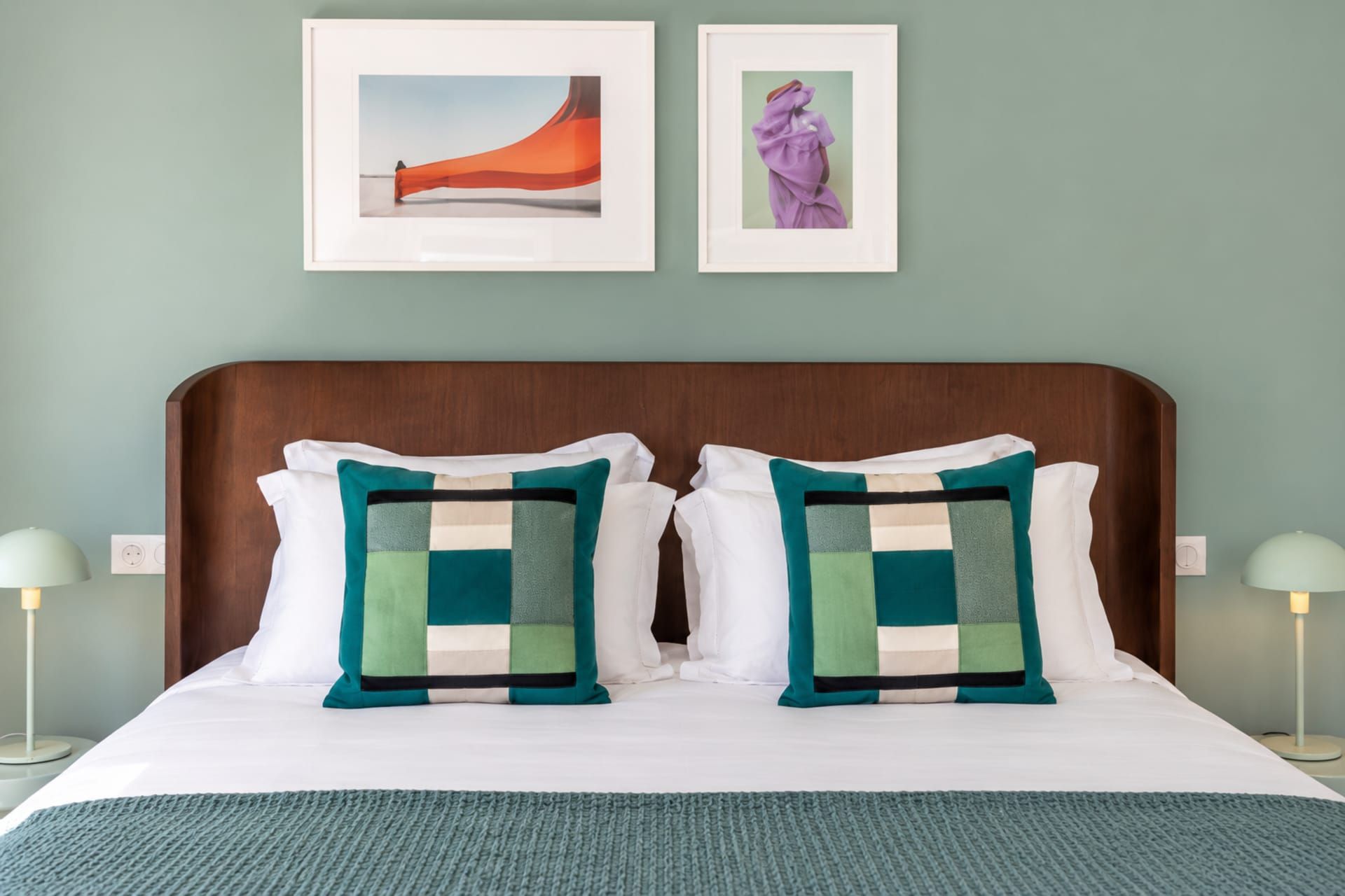 A neatly made bed with two pillows, a wooden headboard, and two bedside lamps.