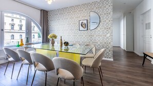 A modern dining area with a glass table, grey upholstered chairs, and a patterned wall.