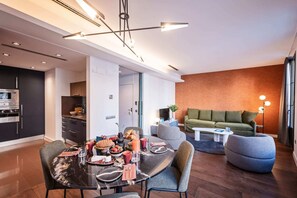 A modern living room with a dining area, featuring a sofa, a coffee table, and a dining table set with food and drinks.
