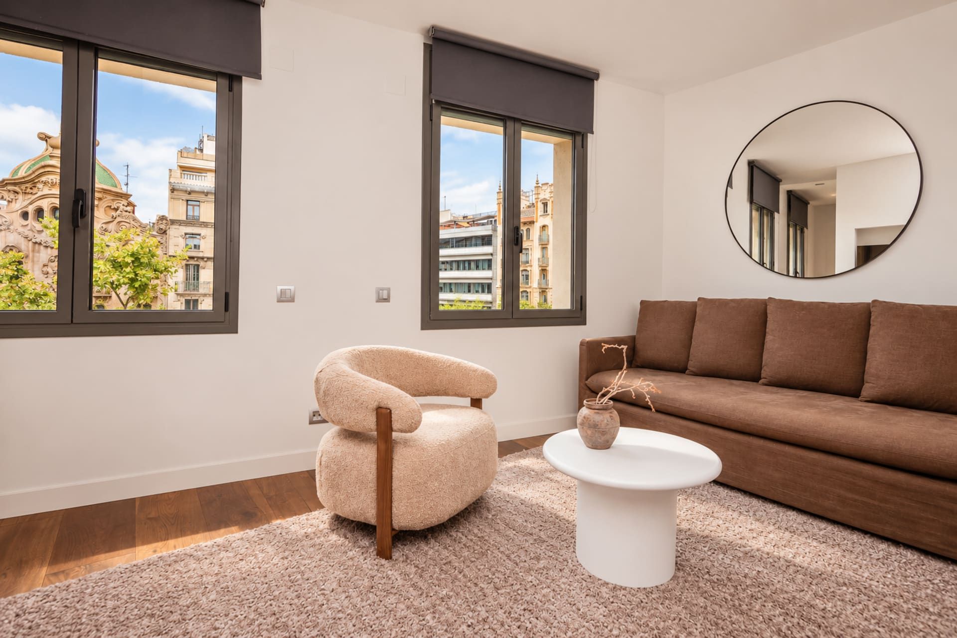 Un salon moderne avec un canapé marron, un miroir rond et un fauteuil beige.