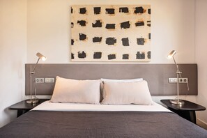 A hotel room with a bed, two bedside tables, a wall-mounted artwork, and two floor lamps.