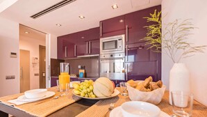 A modern kitchen with purple cabinets, a microwave, and a coffee machine. There is a breakfast setup on the table with bread, fruit, and a glass of orange juice. - Sweett | Palau 601 - One Bedroom Apartment, Sleeps 3 (Barcelona)