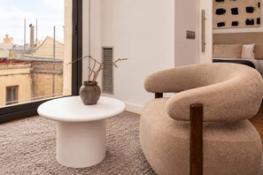 A modern living room with a white round table, a beige armchair, and a view of the cityscape through a large window. - Sweett | Palau 601 - One Bedroom Apartment, Sleeps 3 (Barcelona)