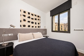 Un dormitorio con una cama grande, un cabecero, un ventanal con vistas a edificios y una obra de arte colgada en la pared.