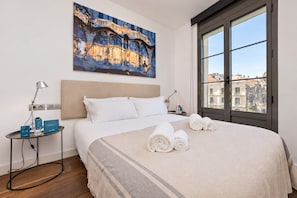 A hotel room with a large bed, a painting above it, and a view of buildings through a large window. - Sweett | Palau 602 - One Bedroom Apartment, Sleeps 3 (Barcelona)