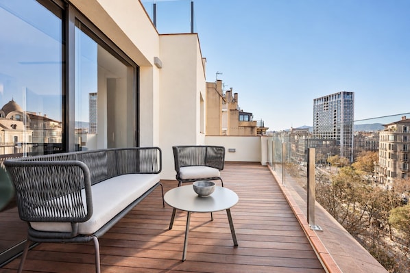 A balcony with a sofa and chairs, a small table, and a view of the cityscape.