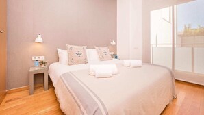 Une chambre à coucher moderne avec un grand lit, deux lampes de chevet, une petite table avec une lampe et une grande fenêtre donnant sur l’extérieur.