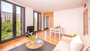 Una sala de estar moderna con un sofá, una mesa de centro con una planta, un televisor y un comedor con sillas y una mesa.