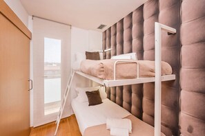 A bunk bed room with a padded headboard, a window, and a door.