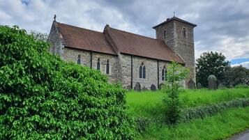 A stone church with a bell tower and arched windows, surrounded by lush greenery and a cemetery.