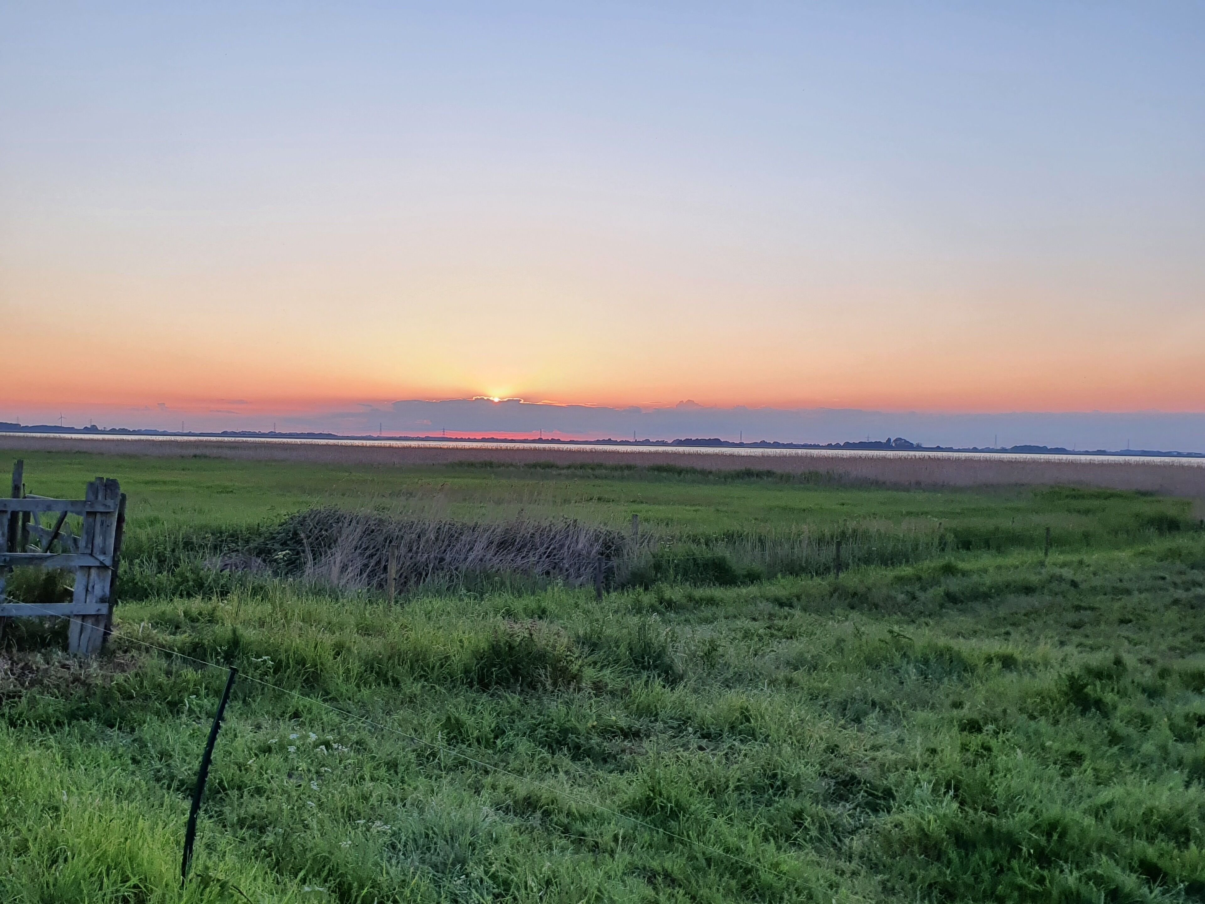 A grassy field with a wooden bench in the foreground and a sunset in the background.