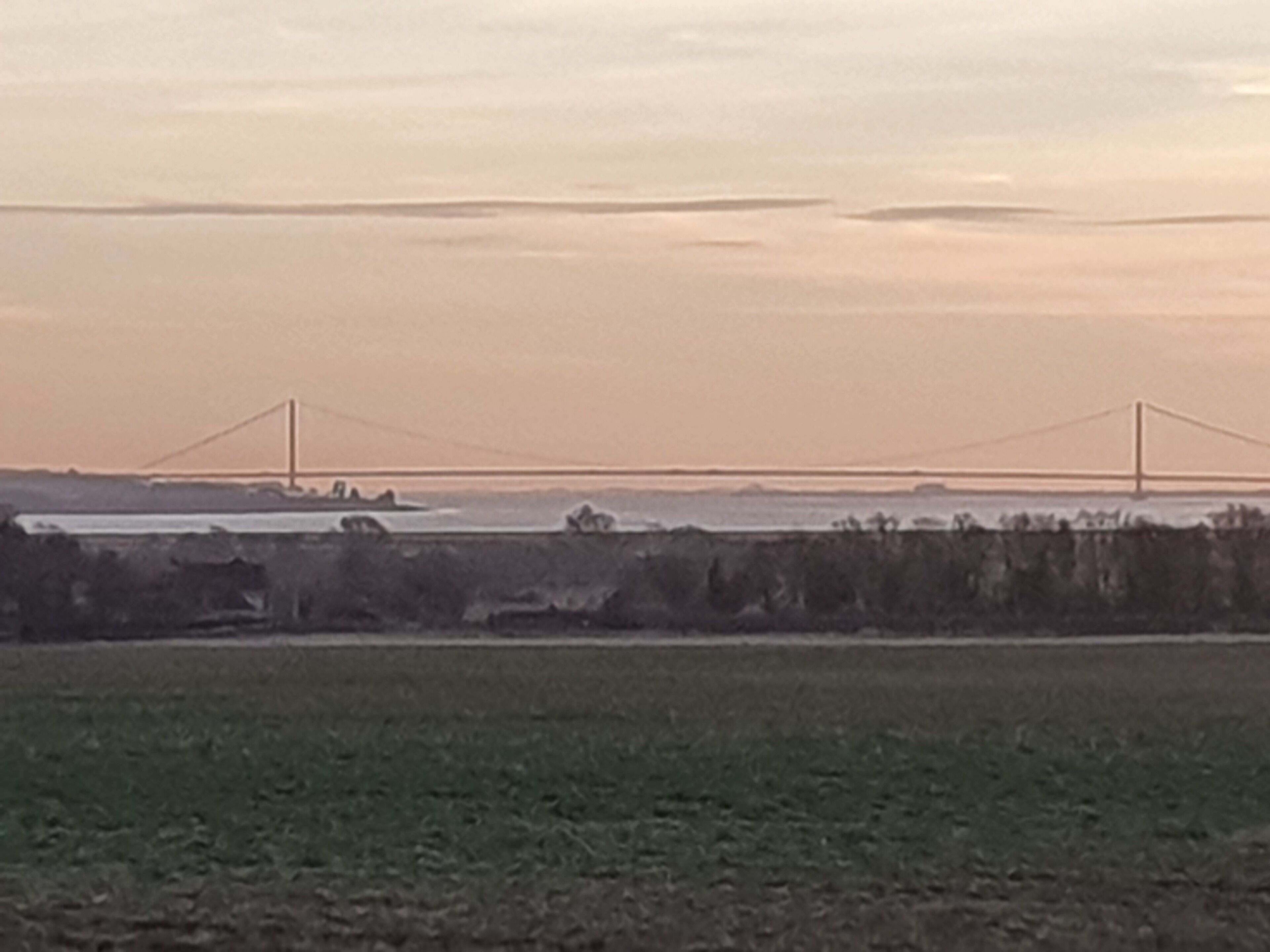 Eine Brücke überspannt einen Fluss, im Vordergrund erstreckt sich eine flache Landschaft.