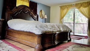 Un dormitorio con una cama de madera, una mesita de noche, un espejo y vistas al exterior a través de una ventana con cortinas.