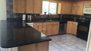 Una cocina con armarios de madera, encimera negra, pileta de acero inoxidable y estufa negra.