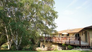 Una casa con terraza, un patio cubierto y un gran árbol en el jardín.
