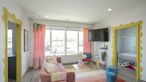 A modern living room with a sofa, a coffee table, a television, and a view of the city through large windows. - 🎸🎇 CLUELESS HOME IN NASH-VEGAS! WALKABLE LOCATION! (Nashville)