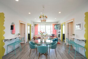 Un espace de salle à manger moderne avec une table en verre, des chaises de couleur turquoise et un lustre central orné de motifs floraux.