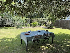 An outdoor dining area with a table set for four, surrounded by greenery and a hedge. - Maison Proche de la Plage (Pornic)