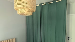 A bedroom with a bed, a nightstand, a green curtain, a wooden headboard, and a wicker hanging light fixture. - Maison Proche de la Plage (Pornic)