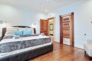 Un dormitorio con una cama grande, suelo de madera y una puerta que da a otra habitación.