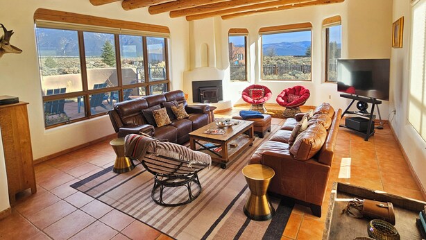 Amplia sala de estar con chimenea, ventanas grandes con vistas a las montañas y un televisor.