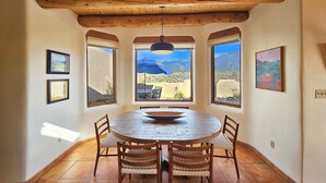 Un comedor con una mesa y sillas de madera, ventanas amplias con vistas a la montaña y obras de arte enmarcadas en las paredes.