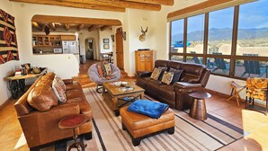 Amplia sala de estar con mobiliario de cuero, techo de madera y grandes ventanales con vistas a la montaña.