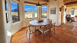 Un comedor con una mesa redonda, sillas de madera y grandes ventanales que ofrecen vistas a la montaña.