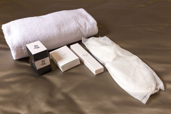A neatly arranged set of toiletries on a bed with a white towel, including a black box, two white boxes, and a white cloth. - Bramble Luxury Suites (Rome)