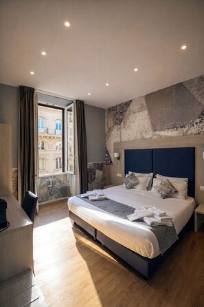 A modern hotel room with a large bed, a desk, and a view of a building through the window. - Bramble Luxury Suites (Rome)