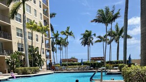 Una piscina con agua cristalina azul, rodeada de palmeras y un edificio de varios pisos con balcones.
