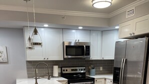 Una cocina moderna con armarios blancos, un refrigerador de acero inoxidable, un microondas y una estufa.