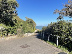 A paved pathway flanked by dense greenery and a metal railing, leading towards a coastal view. - 2-bed, Sleeps 4, Free Parking, Pets Allowed (Eastbourne)